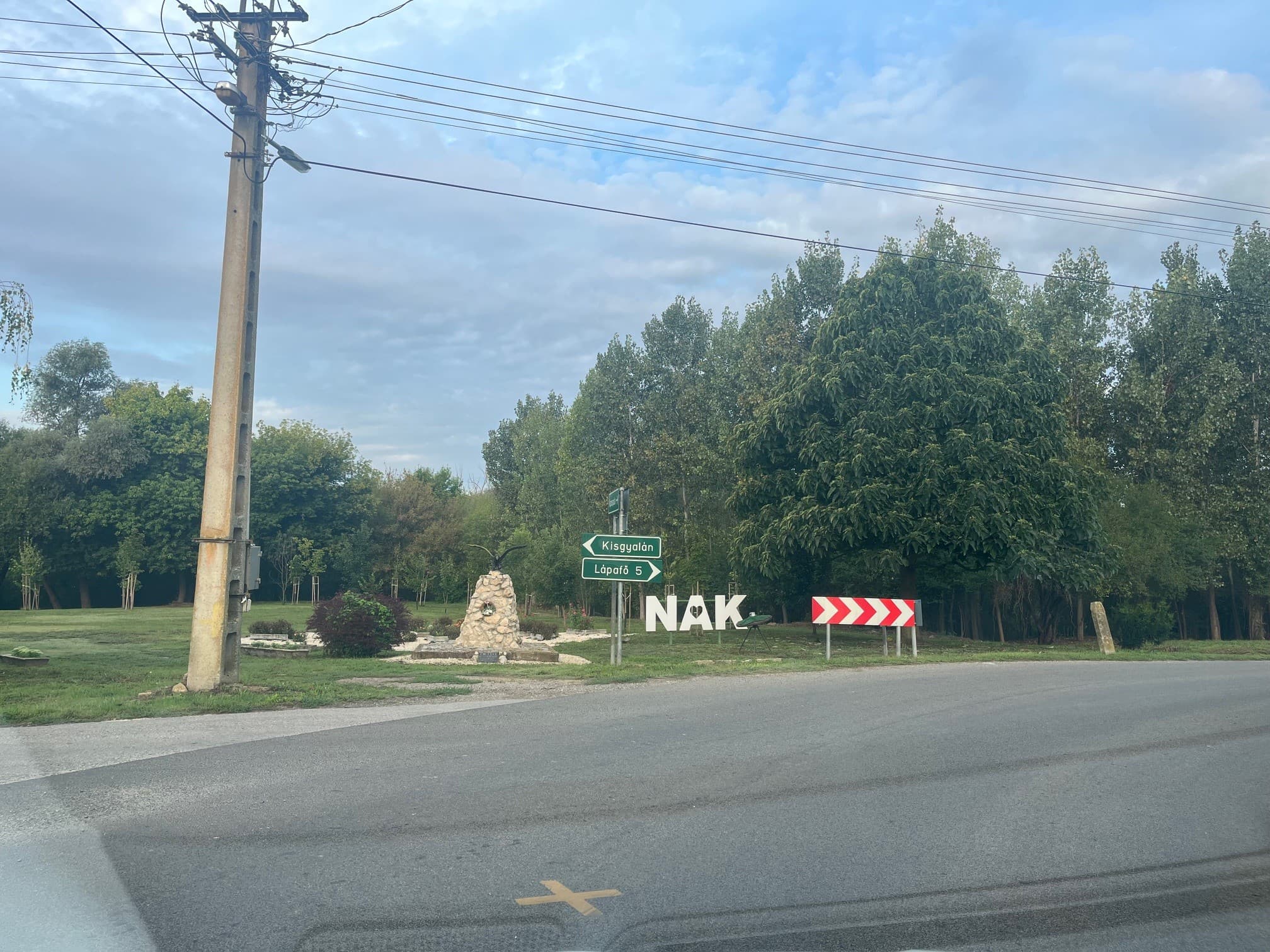 NAK települést jelző tábla fák között